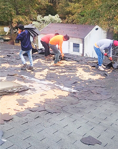 A team of professionals removing an old roof from a large home, with visible progress in stripping away the old materials.